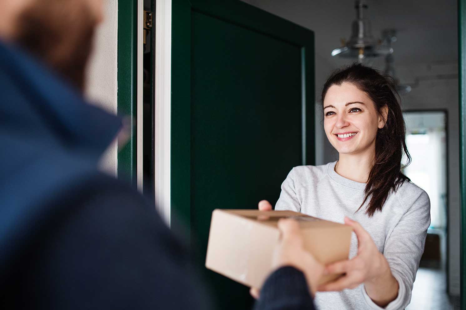 A woman is happy and smiling because she is receiving a parcel from a delivery man at the door.