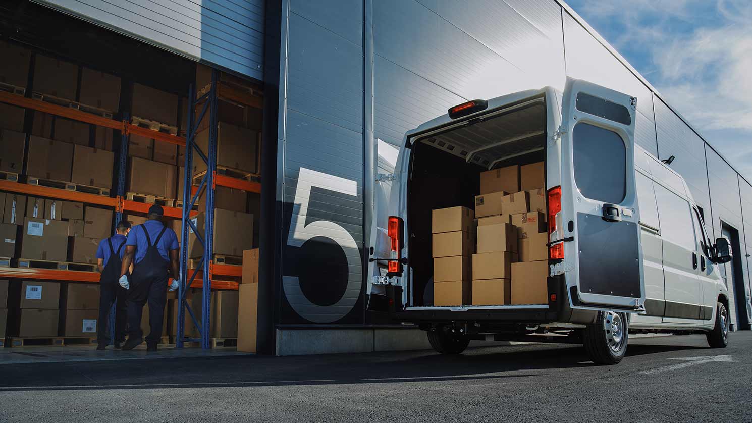 Two couriers loading a delivery van outside a warehouse.