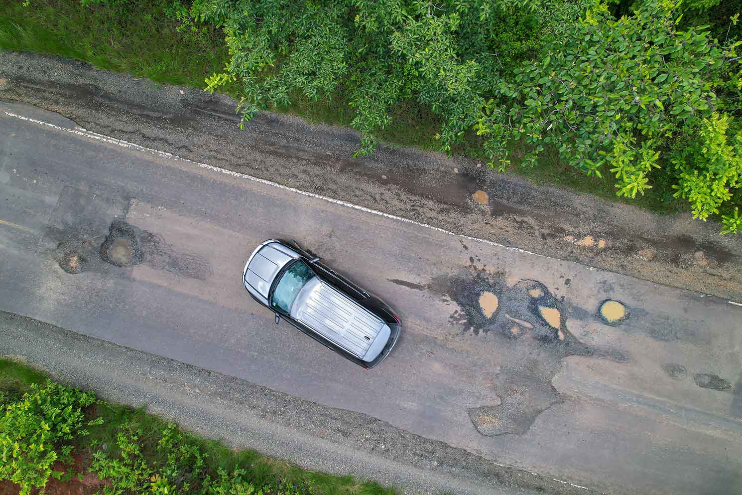 A car driving down the road dodging many large potholes.