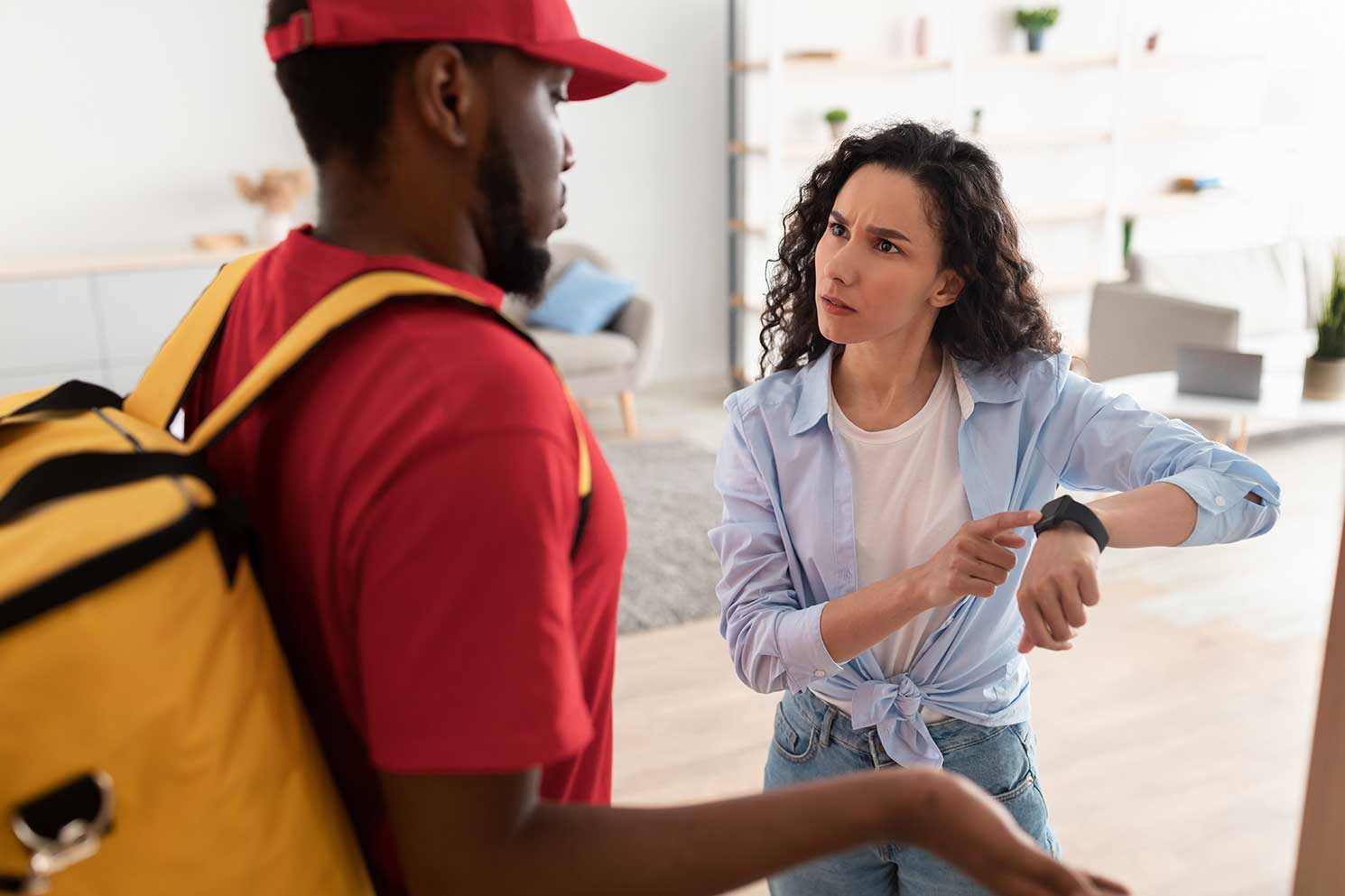 A frustrated customer is receiving her delivery late and indicates that by showing her watch to the delivery driver.