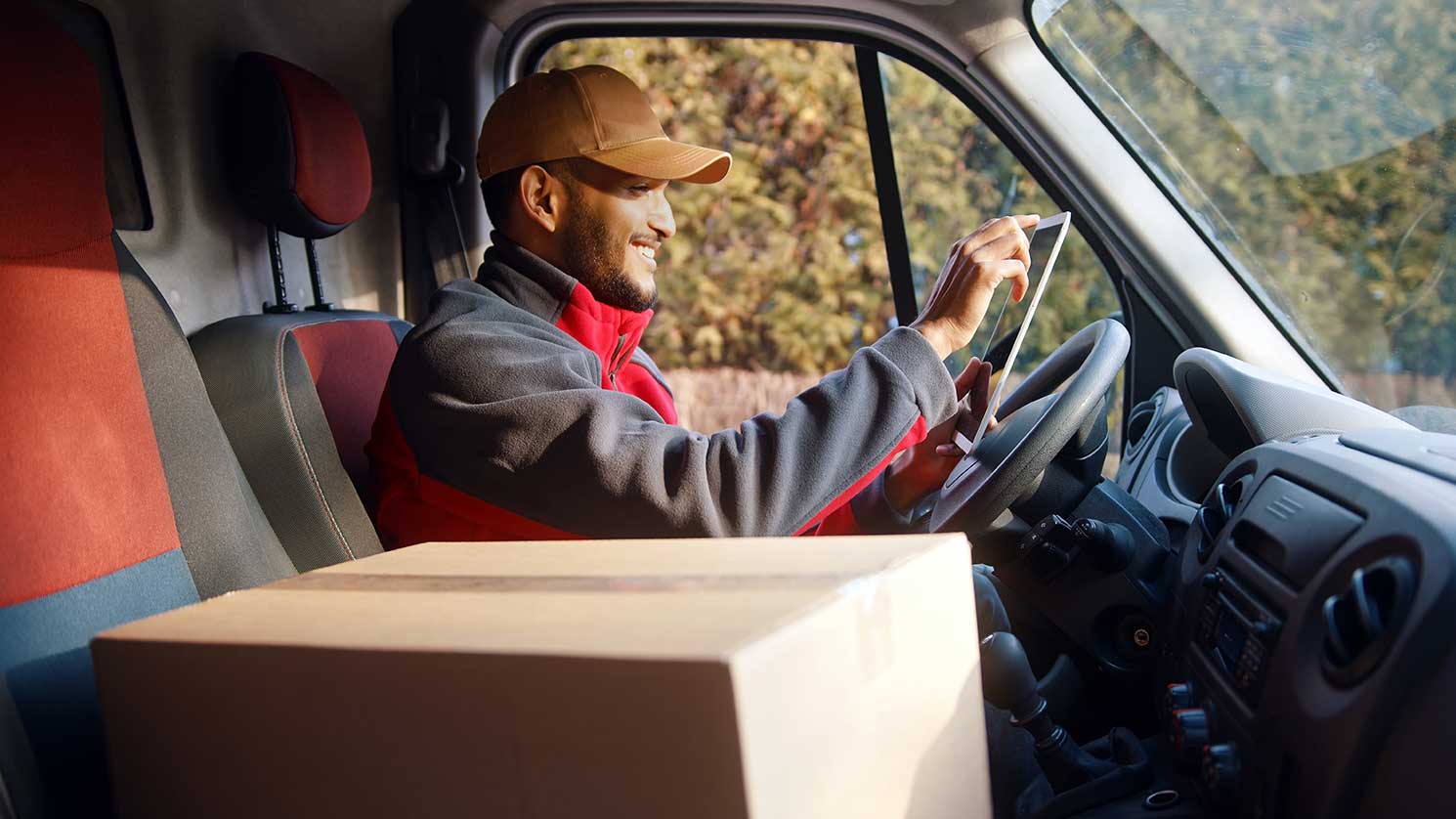 A delivery driver in his van smiling while using mobile courier software.